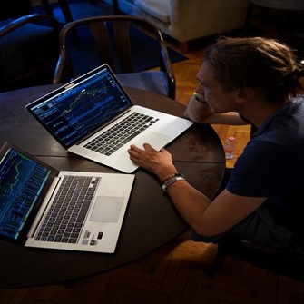 Ein Mann sitzt vor zwei Laptops und handelt mit Vermögenswerten.